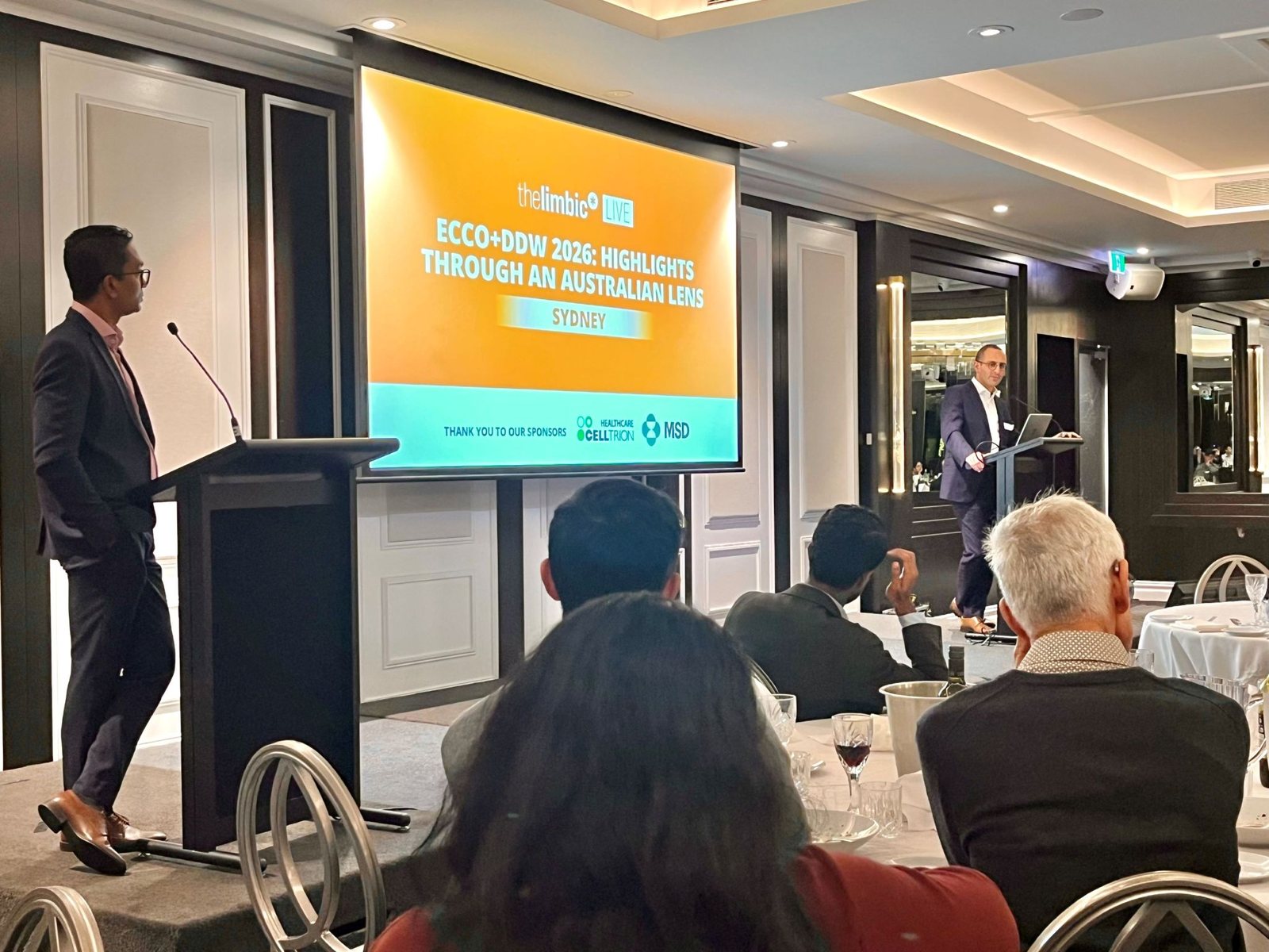 A/Prof Viraj Kariyawasam at the lectern chairing the limbic LIVE meeting in Sydney, with the ECCO and DDW 2026 title slide on screen